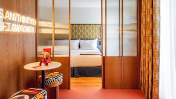 Una habitación de hotel con una cama, una mesita con un florero y una pared con un letrero.