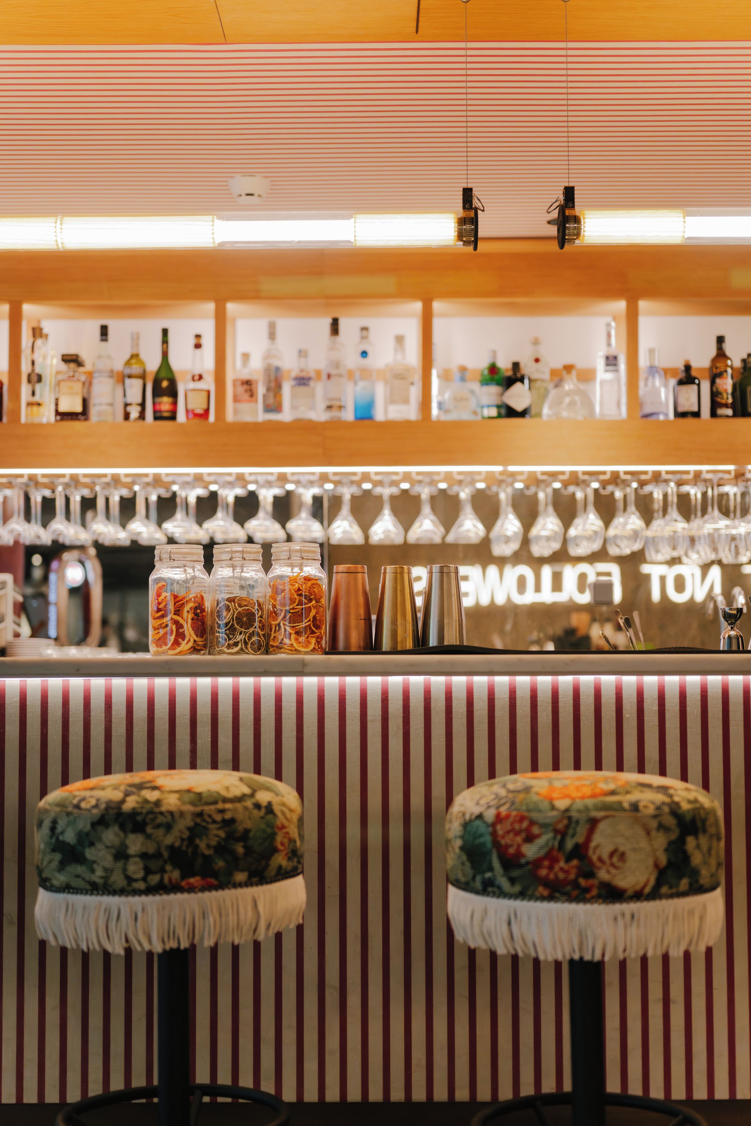 A bar area with striped seating, a variety of bottles on shelves, and hanging glasses.
