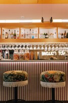 Una zona de bar con asientos a rayas, una variedad de botellas en estantes y copas colgando.