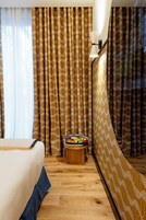 A hotel room with a bed, a small wooden table, and a mirror reflecting the room's decor.