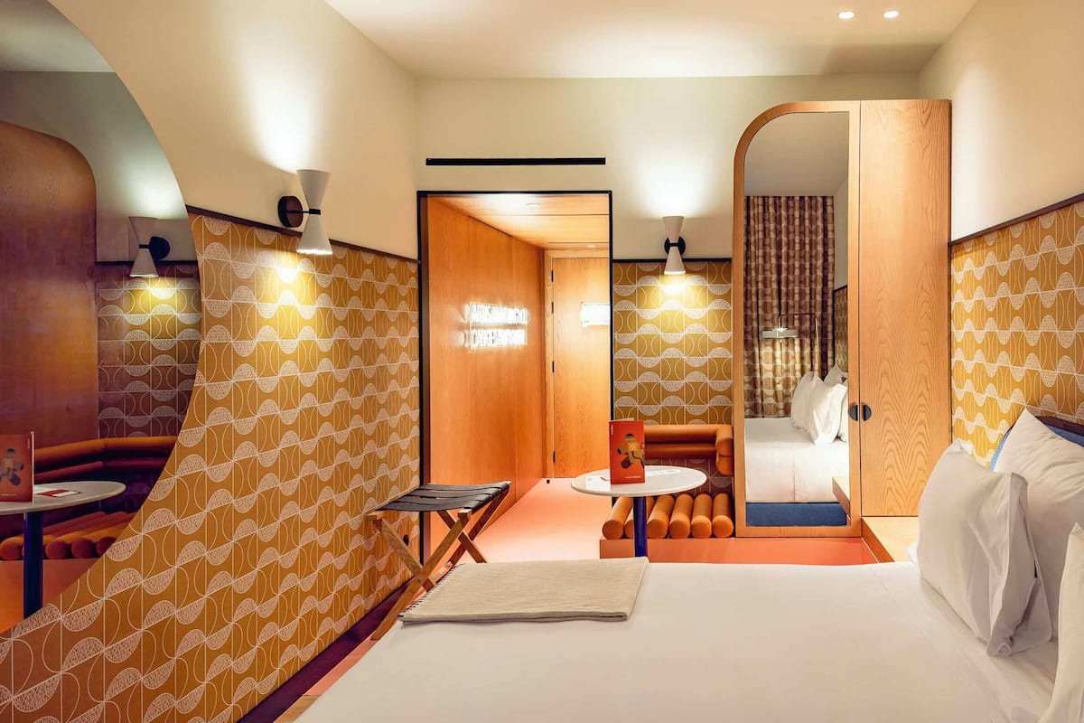 Una habitación de hotel con una cama, una mesita, una zona de estar y un espejo.