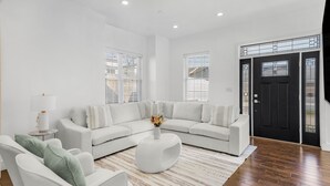 A modern living room with a sectional sofa, a round coffee table, and a large window with blinds. - Elegant Open Concept Close To DC (Arlington)