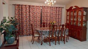 A dining room with a table, chairs, a cabinet, and curtains.