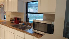 Eine Küche mit weißen Schränken, einer Edelstahl-Spüle, einer roten Kaffeemaschine und einer Mikrowelle.
