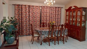Een eetkamer met een ronde tafel, stoelen, een kast en gordijnen.