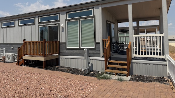 A modern mobile home with a covered porch, a small outdoor seating area, and a visible air conditioning unit.