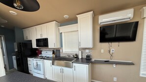 A modern kitchen with white cabinets, a stainless steel stove, a microwave, and a flat-screen TV mounted on the wall.