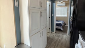 A hallway with a white wardrobe, a trash bin, a bed with a blue and white patterned bedspread, and a black refrigerator.