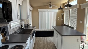A modern kitchen with white cabinetry, a black microwave, a stove, and a ceiling fan.