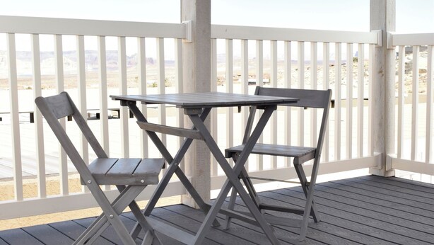 A covered outdoor area with a wooden table and two chairs, a white railing, and a view of a desert landscape.