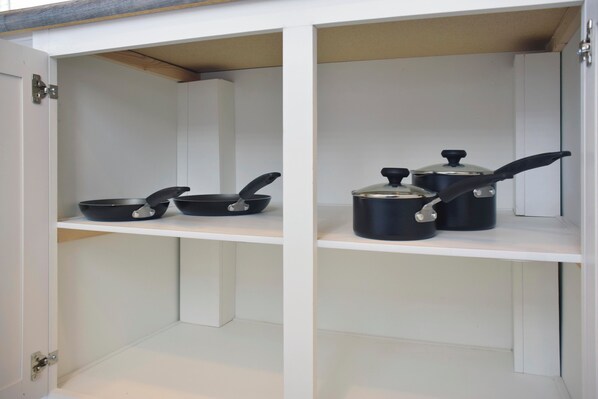 Una cocina con armarios blancos y encimera blanca. Hay dos sartenes negras y una olla negra con tapa sobre la encimera.