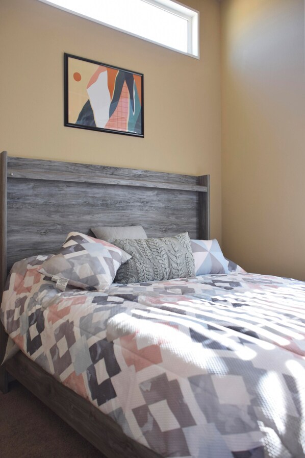 Un dormitorio con cama, almohadas y un cuadro abstracto colgado en la pared.