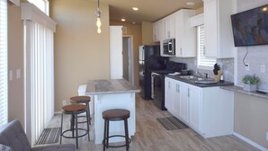 A modern kitchen with white cabinets, a central island with stools, a built-in oven, and a TV mounted on the wall.