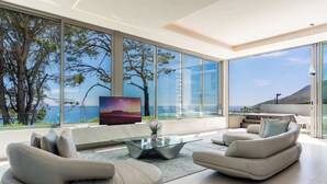 Una sala moderna con una mesa de centro de vidrio, sofás color beige y un televisor grande.