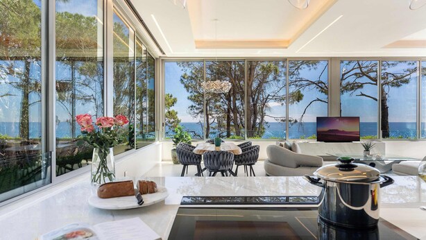 Una cocina moderna con un ventanal grande con vista al mar, un comedor con mesa y sillas, y una cafetera en la encimera.