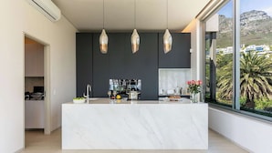 Cocina moderna con una isla de mármol, luces colgantes y vistas a la montaña.