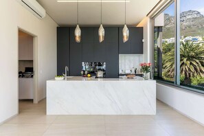 Une cuisine moderne dotée d’un îlot en marbre, de luminaires suspendus et offrant une vue sur une montagne.