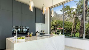 Una cocina moderna con una isla grande, muebles oscuros y vistas a árboles y montañas.