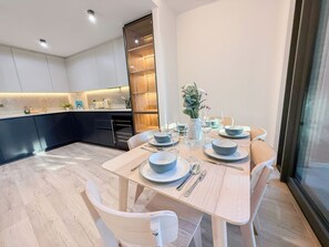 Una cocina moderna con armarios oscuros, una mesa de comedor de madera con platos, cuencos y cubiertos, y un jarrón con flores.