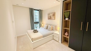 A modern bedroom with a bed, bedside tables, a wardrobe, and a window with curtains. - Elegant 2-BR Flat w/ Lift & Private Balcony – Farringdon, Clerkenwell, Barbican (London)