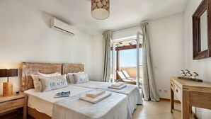 Een slaapkamer met twee bedden, een houten hoofdbord, een nachtkastje met een lamp, een houten dressoir en uitzicht op de omgeving.
