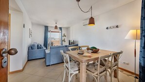 Een moderne woonkamer met een eettafel, stoelen, een bank en uitzicht op buiten.