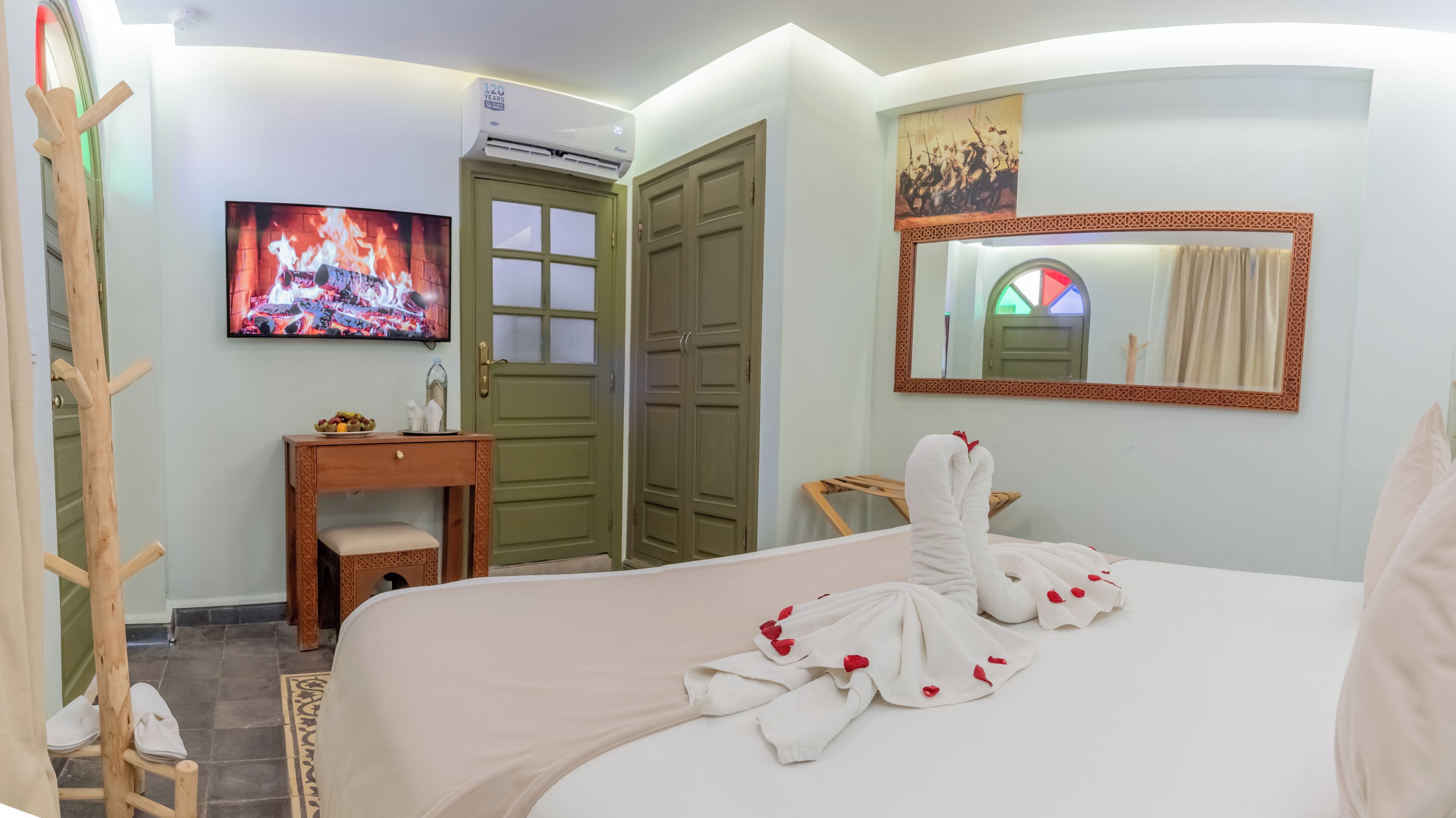 A hotel room with a bed, a TV, a desk, a wardrobe, and a mirror.