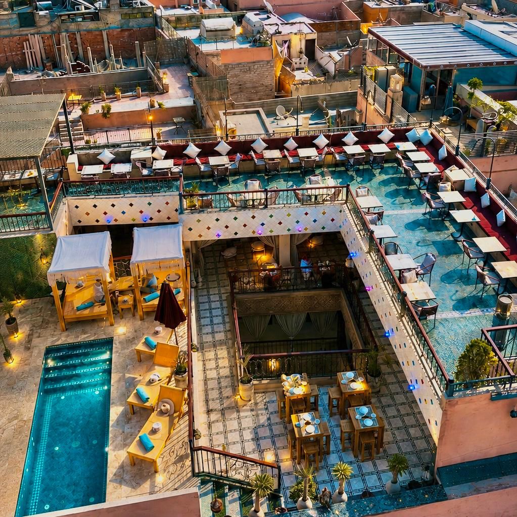 A rooftop bar with outdoor seating, a swimming pool, and a view of the surrounding buildings.