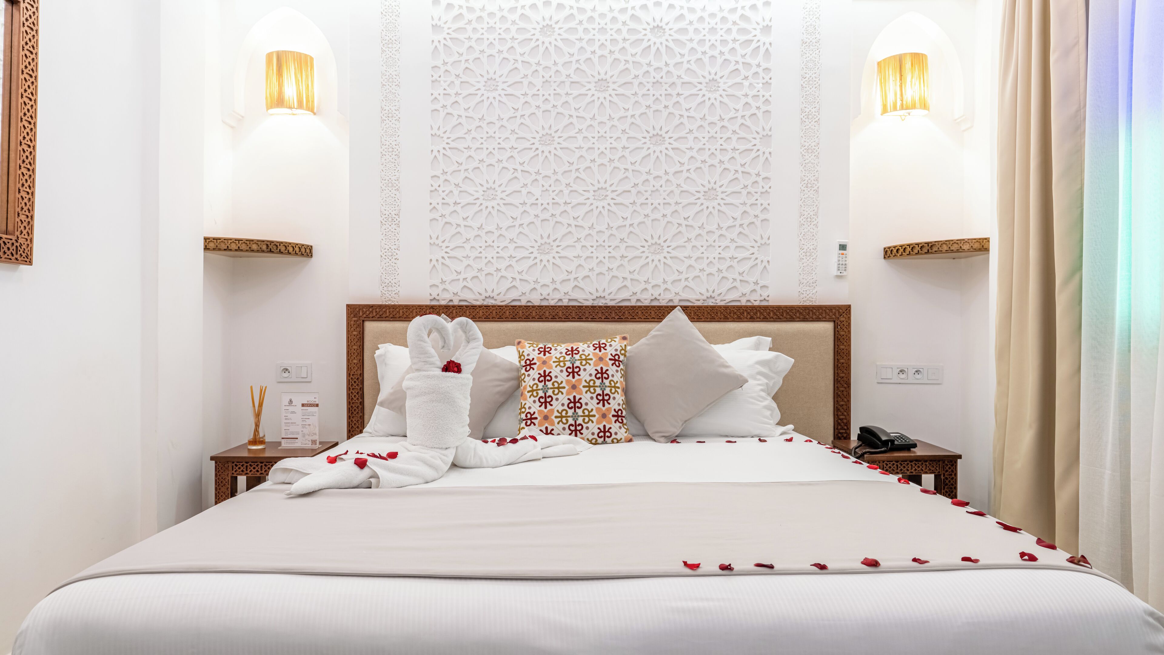 Habitación de hotel con una cama bien hecha, un cabecero decorativo, dos apliques de pared y un panel decorativo sobre la cama.
