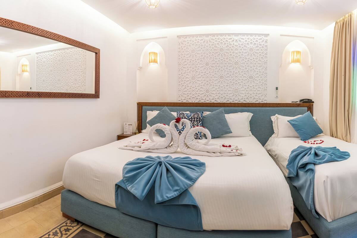 A hotel room with two beds, a large mirror, decorative wall panels, and a view of the sea through the window.