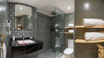 Un baño moderno con un salpicadero de azulejos blanco y negro, cabina de ducha de vidrio y estantes de madera con toallas blancas.
