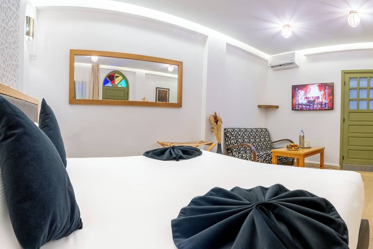 A hotel room with a bed, a chair, a small table, a TV, and a green door.