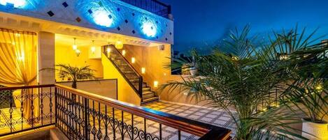 A hotel with a staircase leading to a balcony, a pool area, and palm trees.