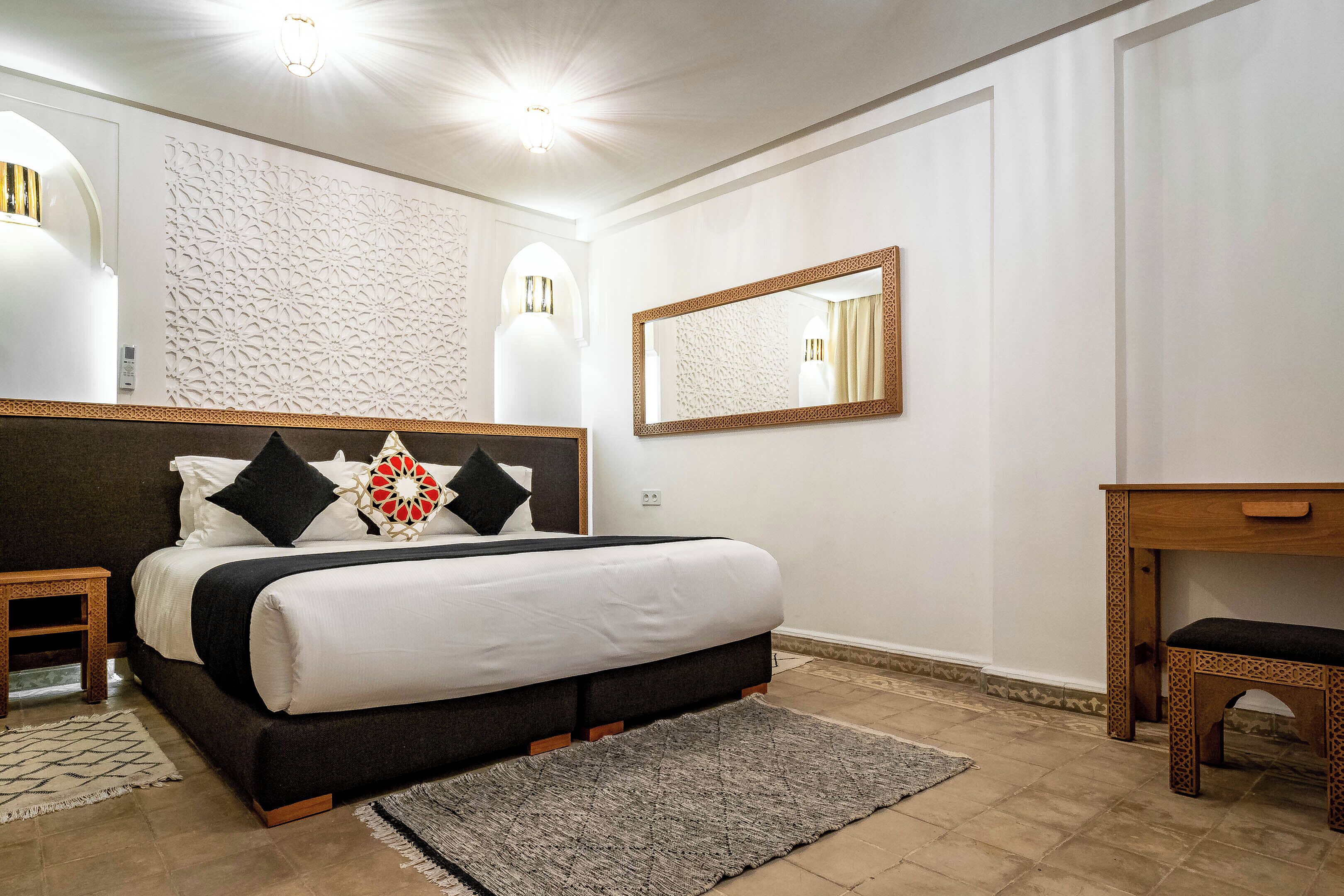 Een moderne slaapkamer met een groot bed, een nachtkastje, een houten bankje en een spiegel aan de muur.