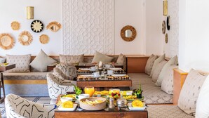 A cozy living room with a sofa set, a coffee table with breakfast items, and decorative wall art. -  Riad Hamdane Rooftop & SPA  (Marrakech)