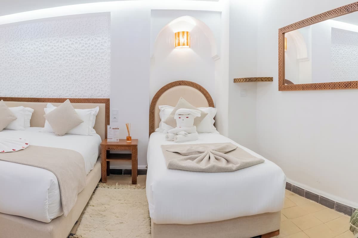 A hotel room with two beds, a wooden desk, a small table with fruit, and a decorative wall piece.