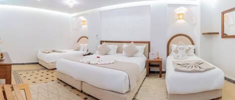 Habitación de hotel con dos camas, un escritorio de madera, una mesita con fruta y un adorno en la pared.