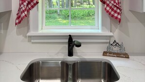 A kitchen with a window, a stainless steel sink, and a decorative sign above the sink. - Cozy Country Cottage in Sullivan County Catskills. 2 Bedrooms, 1 Bath, Heat & AC (Ferndale)