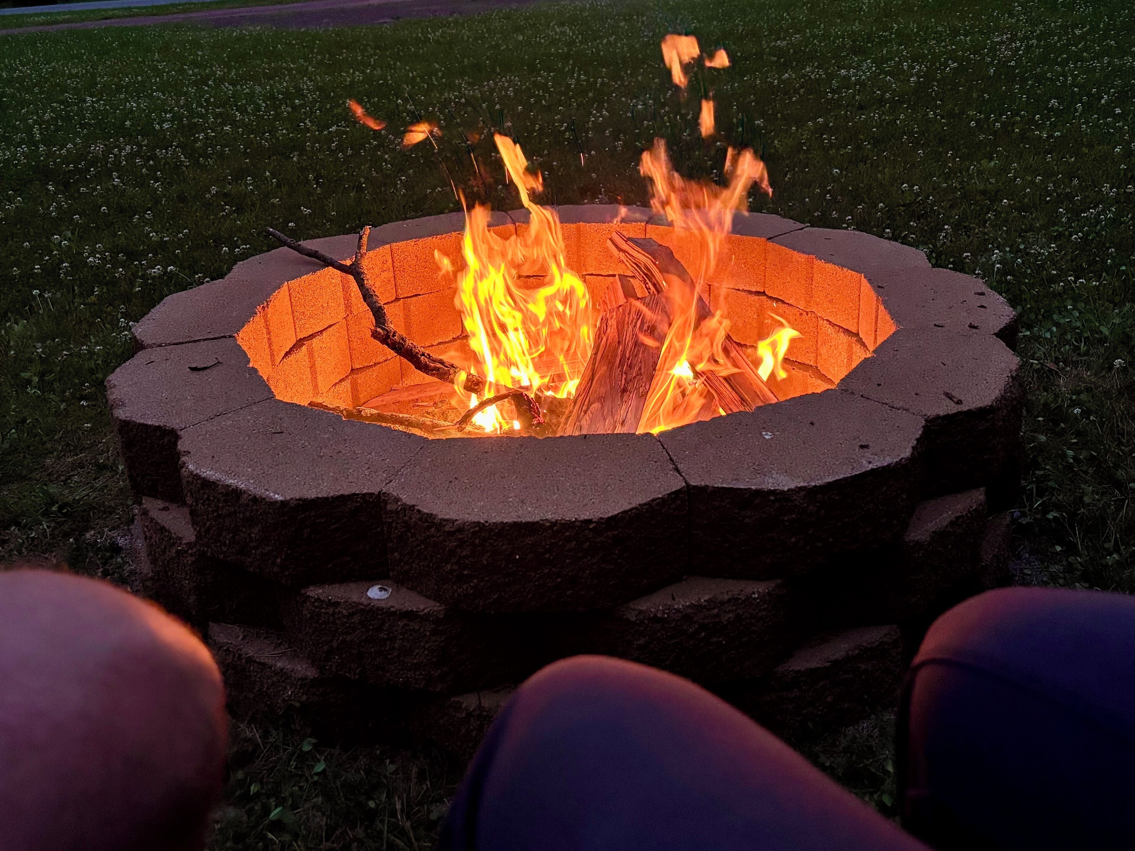 A circular fire pit with flames, surrounded by grass.