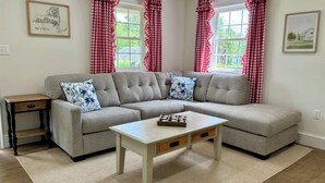 A living room with a sectional sofa, a small side table, a coffee table, and red and white checkered curtains. - Cozy Country Cottage in Sullivan County Catskills. 2 Bedrooms, 1 Bath, Heat & AC (Ferndale)