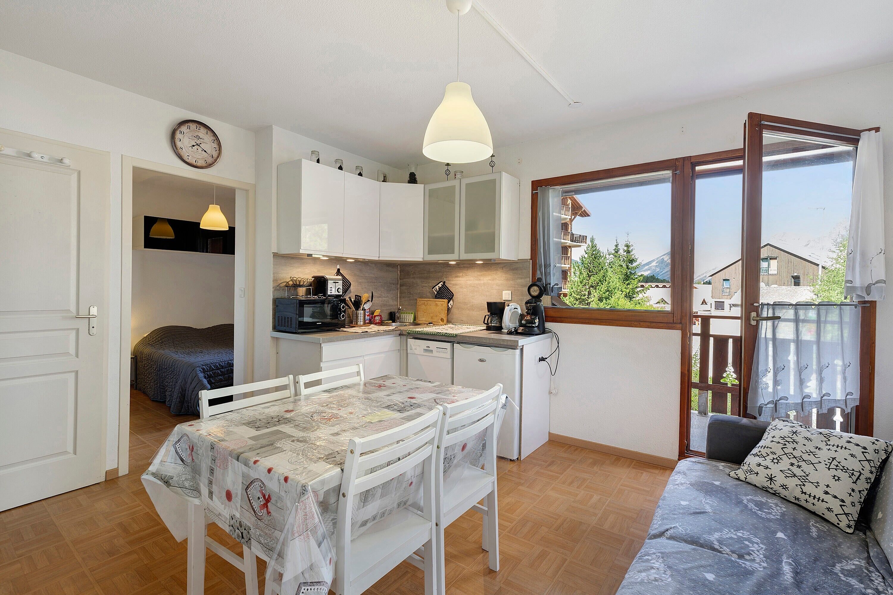 Une cuisine compacte comprenant un coin repas, un petit réfrigérateur et une fenêtre donnant sur des immeubles.
