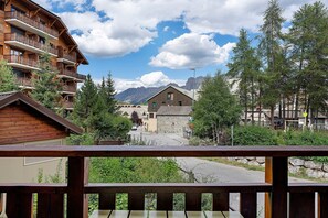 En byggnad av trä med balkonger, en byggnad av sten med ett sadeltak och en bergskedja i bakgrunden.