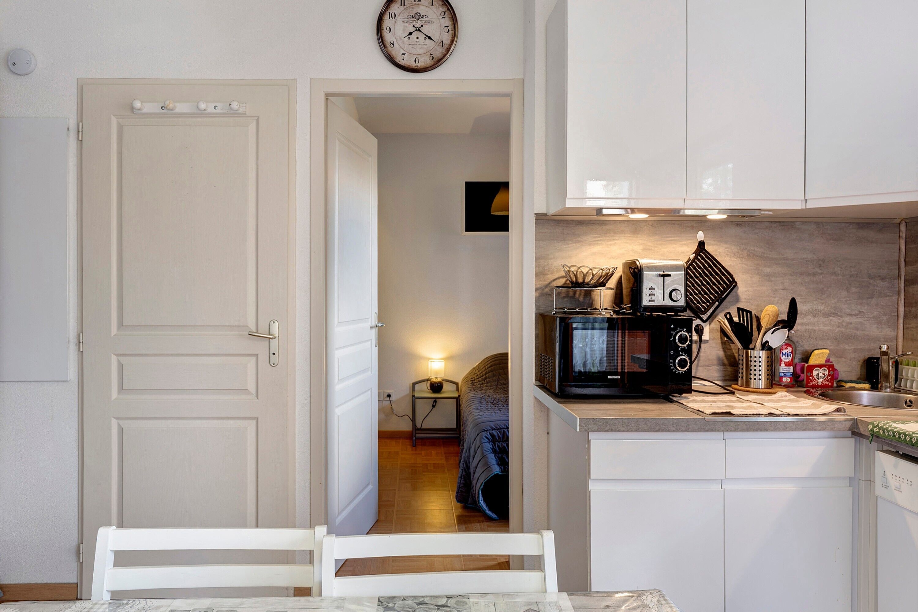 A compact kitchen with white cabinetry, a microwave, and a small table with chairs.