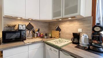 A compact kitchen with white cabinets, a microwave, a toaster, a coffee maker, and a kettle.
