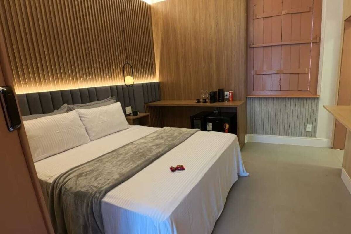 A hotel room with a large bed, a bedside table, a desk, a television, and a wall-mounted shelf.