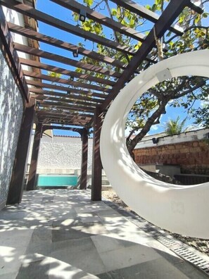 A covered outdoor area with a pergola structure, a circular white object, and a stone wall in the background. - Encantos Pousada Boutique (Pirenopolis)