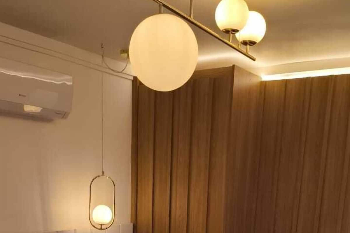 A neatly made bed with a grey blanket, a bedside table with a lamp, and a wooden panel wall.