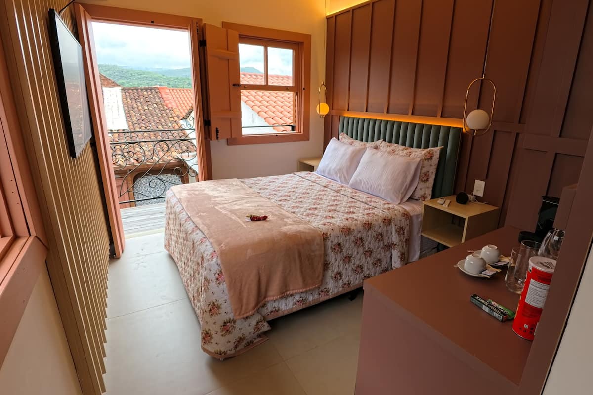 A bedroom with a bed, bedside table, and a view of a balcony.