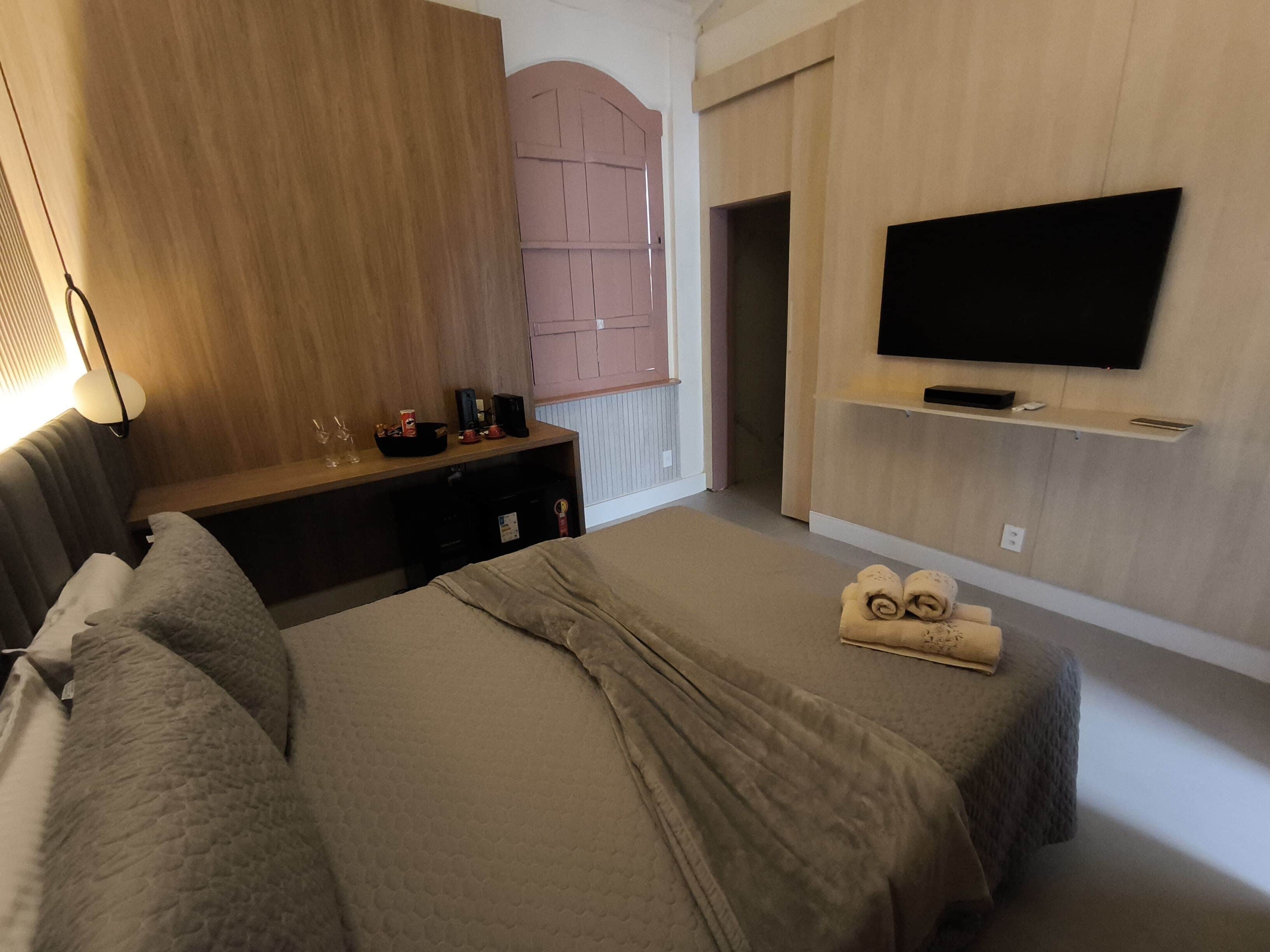 A hotel room with a bed, a desk, a TV mounted on the wall, and a window with a view.