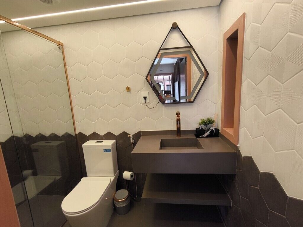 A modern bathroom with a hexagonal mirror, a toilet, and a sink with a dark countertop.